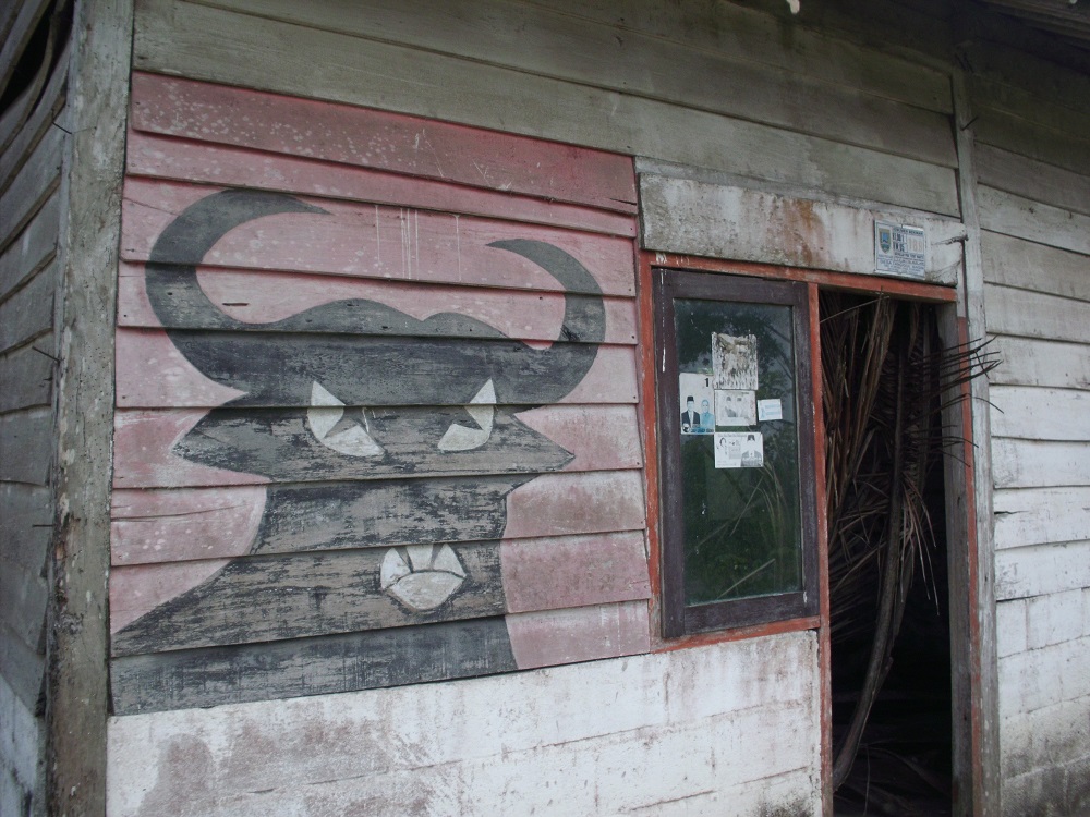 An ex-transmigrant's house in Kampung Eksodan. (Laila Kholid Alfirdaus) The worn-down, wooden-plank exterior of a house, bare but for a mural of a bull on a red background - PDI-P's symbol. (Laila Kholid Alfirdaus)